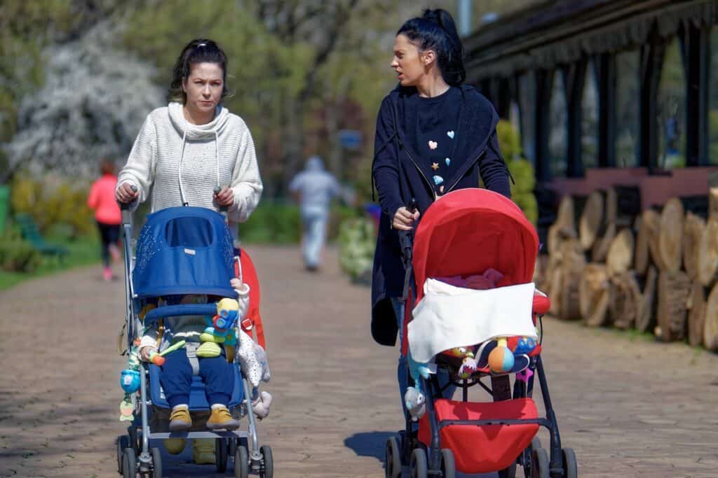 two women walking with their children in the strollers