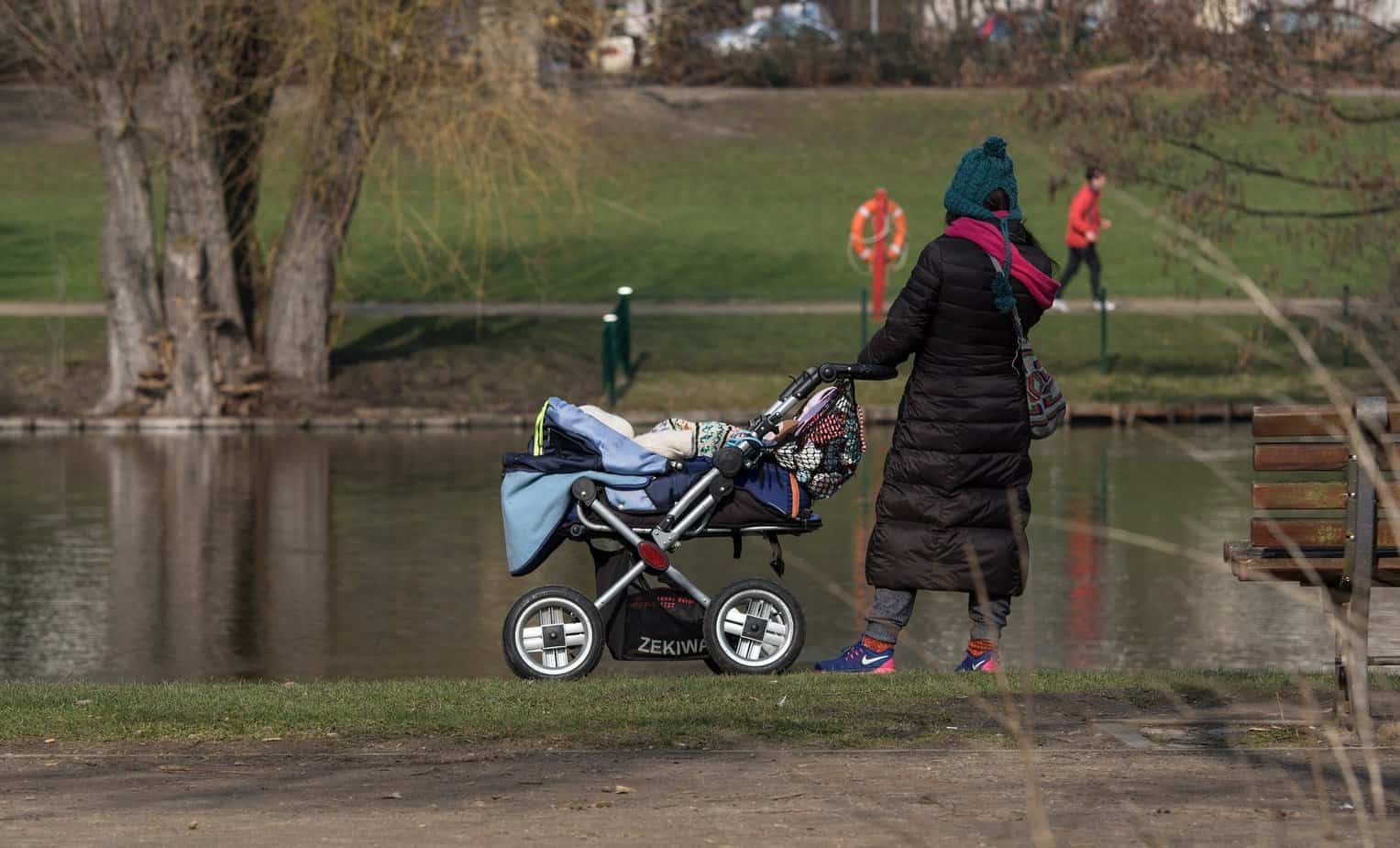 woman walking with the blue stroller near the lake 