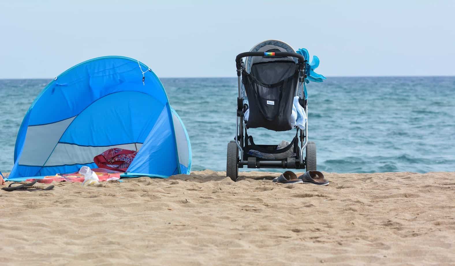 Stroller with Blanket inside standing on the beach near the blue tent