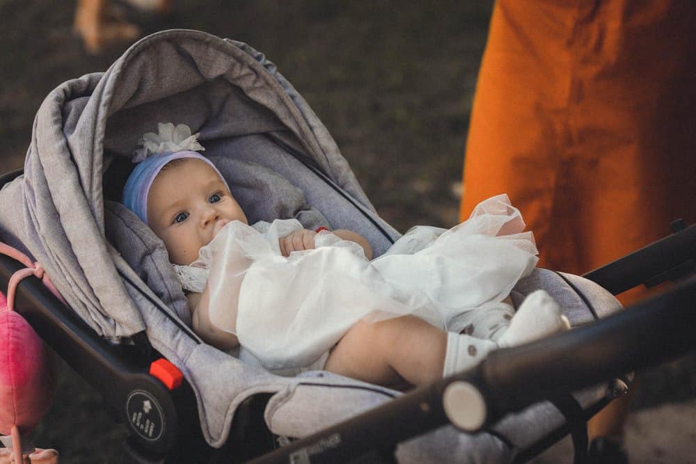 baby in a white dress lies in a stroller