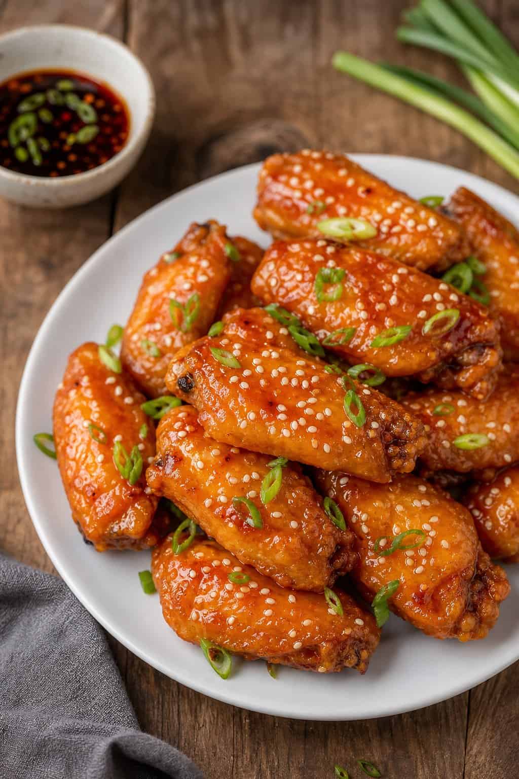 A plate of orange-glazed Chinese-style chicken wings garnished with green onions and sesame seeds on a wooden table.