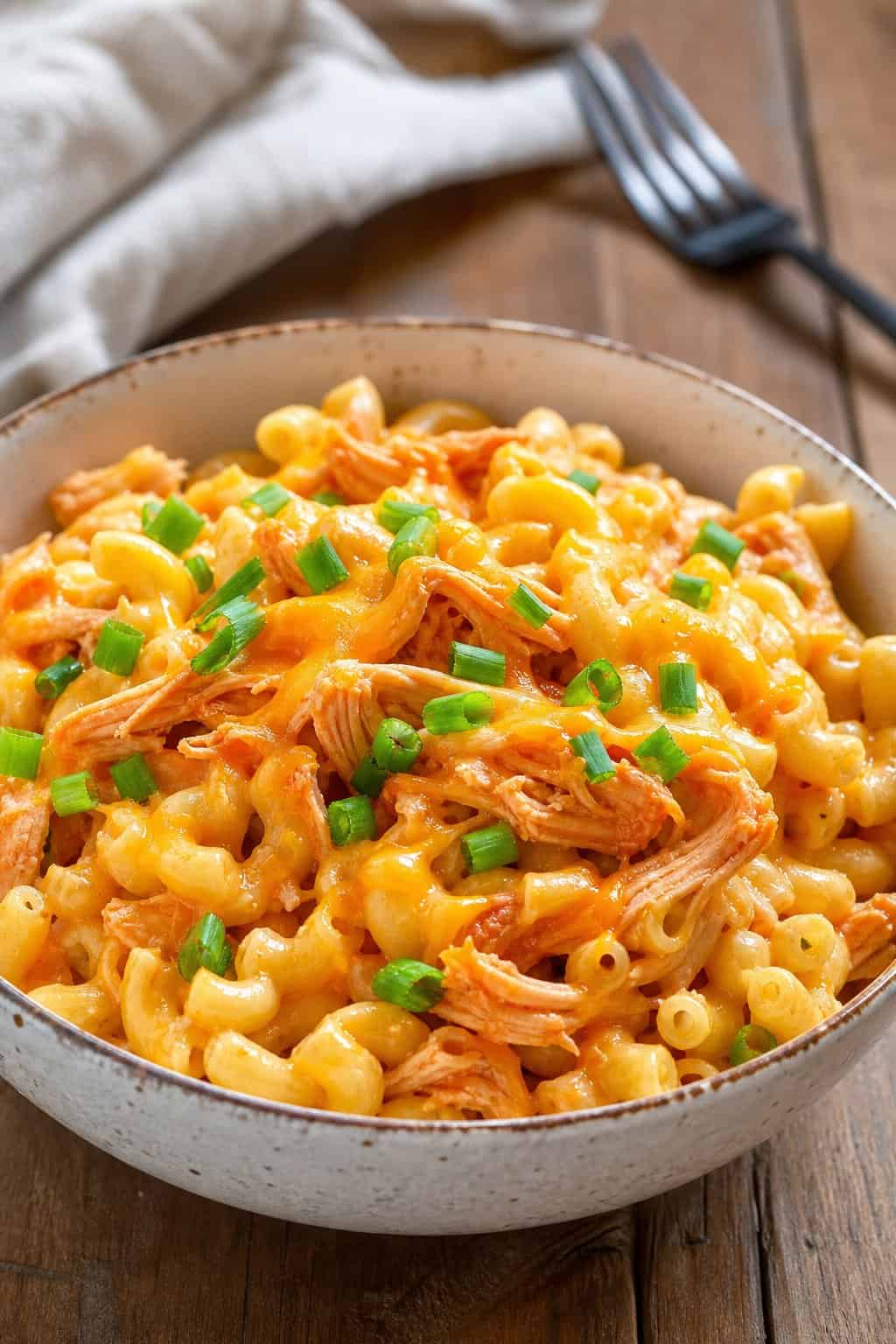 A bowl of buffalo chicken mac and cheese garnished with green onions on a wooden table.