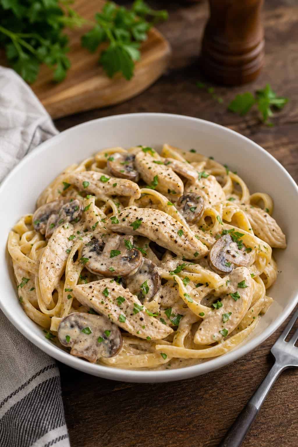 A bowl of creamy mushroom chicken stroganoff pasta garnished with parsley on a wooden table.