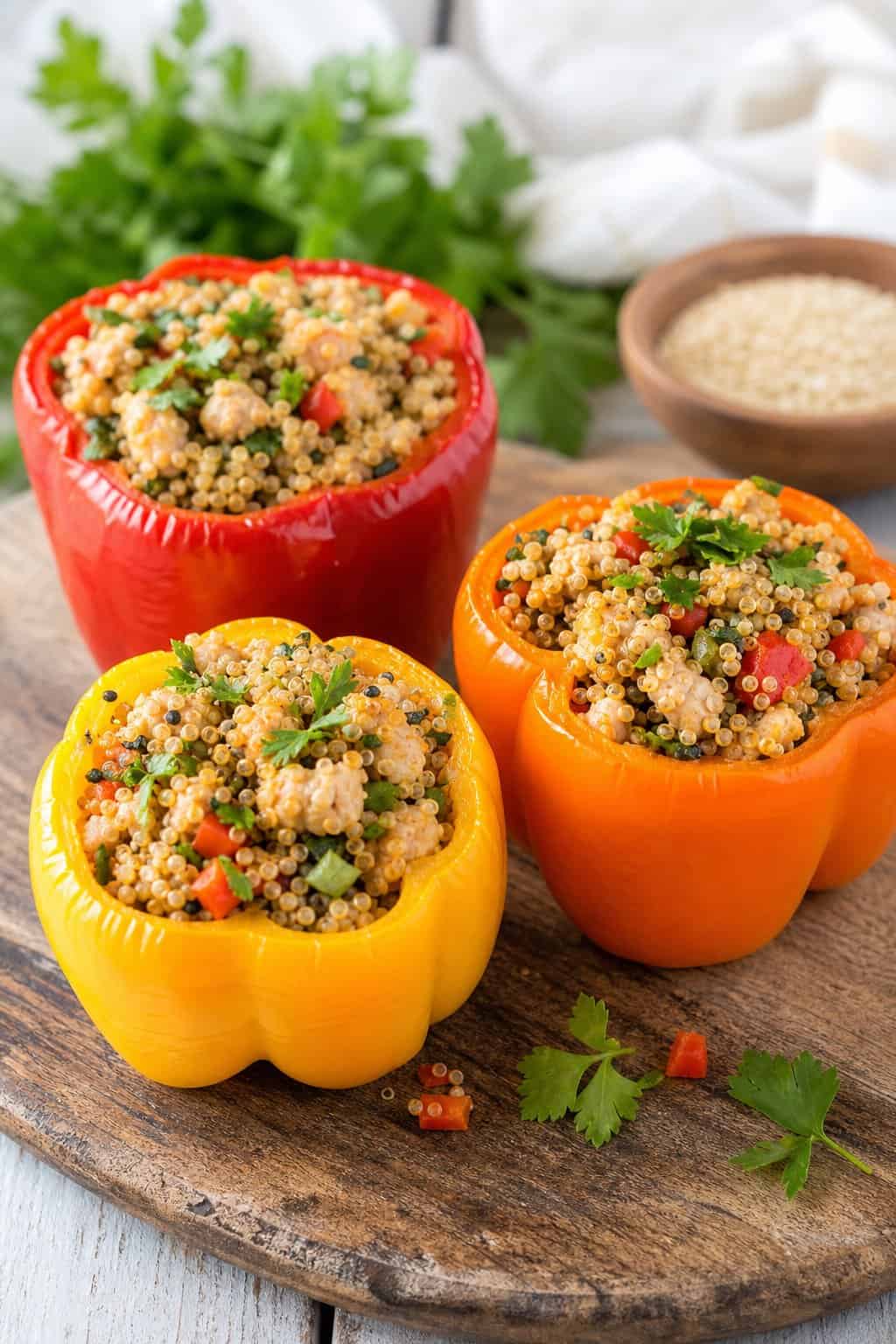 Three colorful bell peppers stuffed with minced chicken and quinoa on a wooden cutting board.