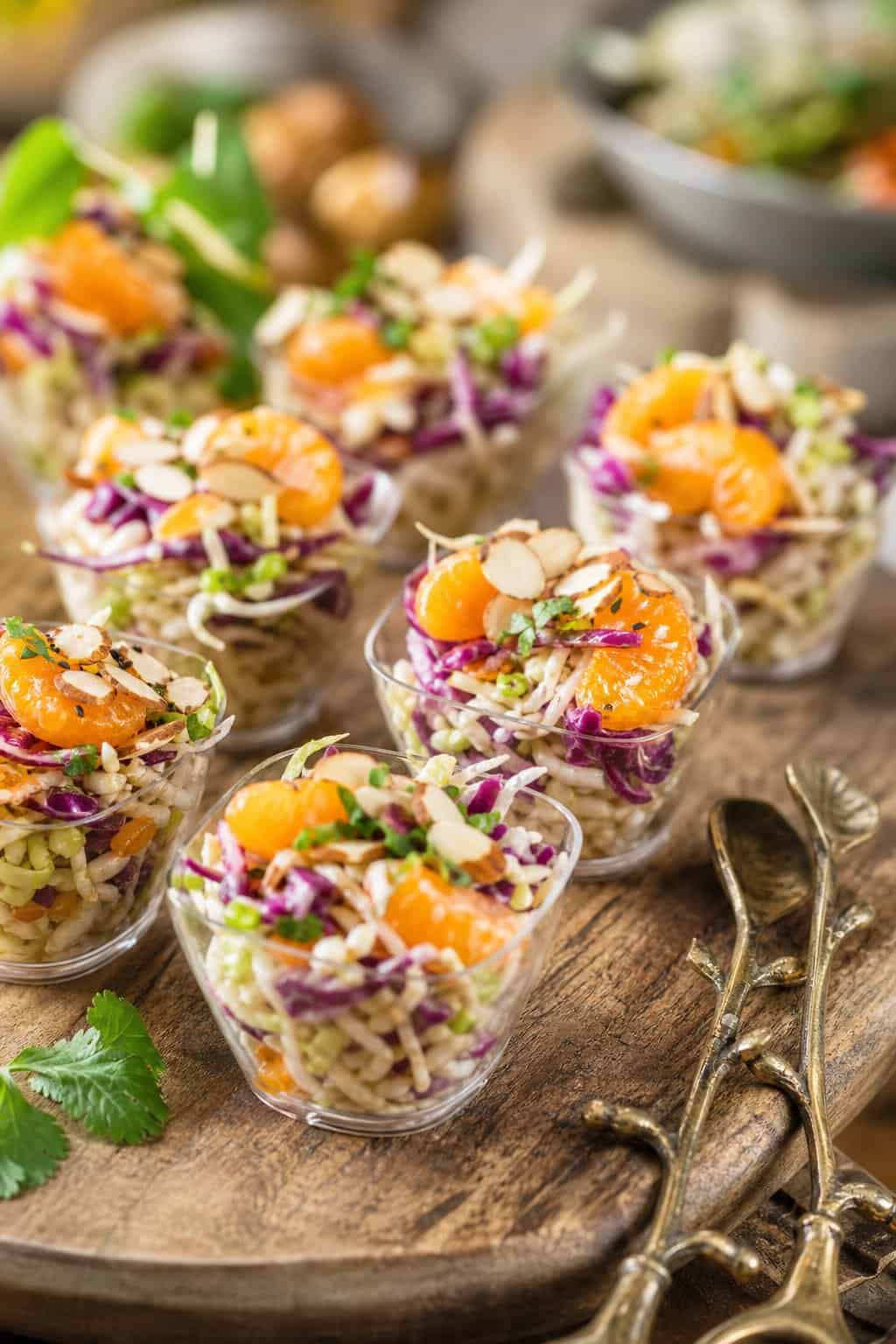 Individual cups of Asian slaw with mandarin oranges and almonds arranged on a wooden serving board.