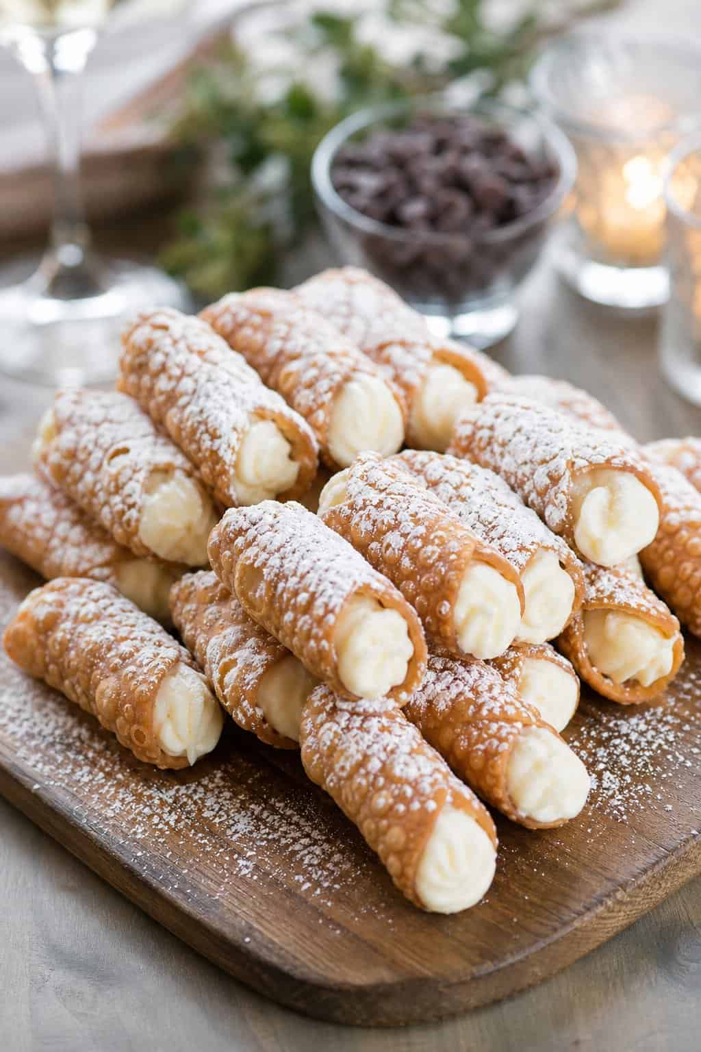 A plate of mini cannoli dusted with powdered sugar arranged on a wooden serving board.