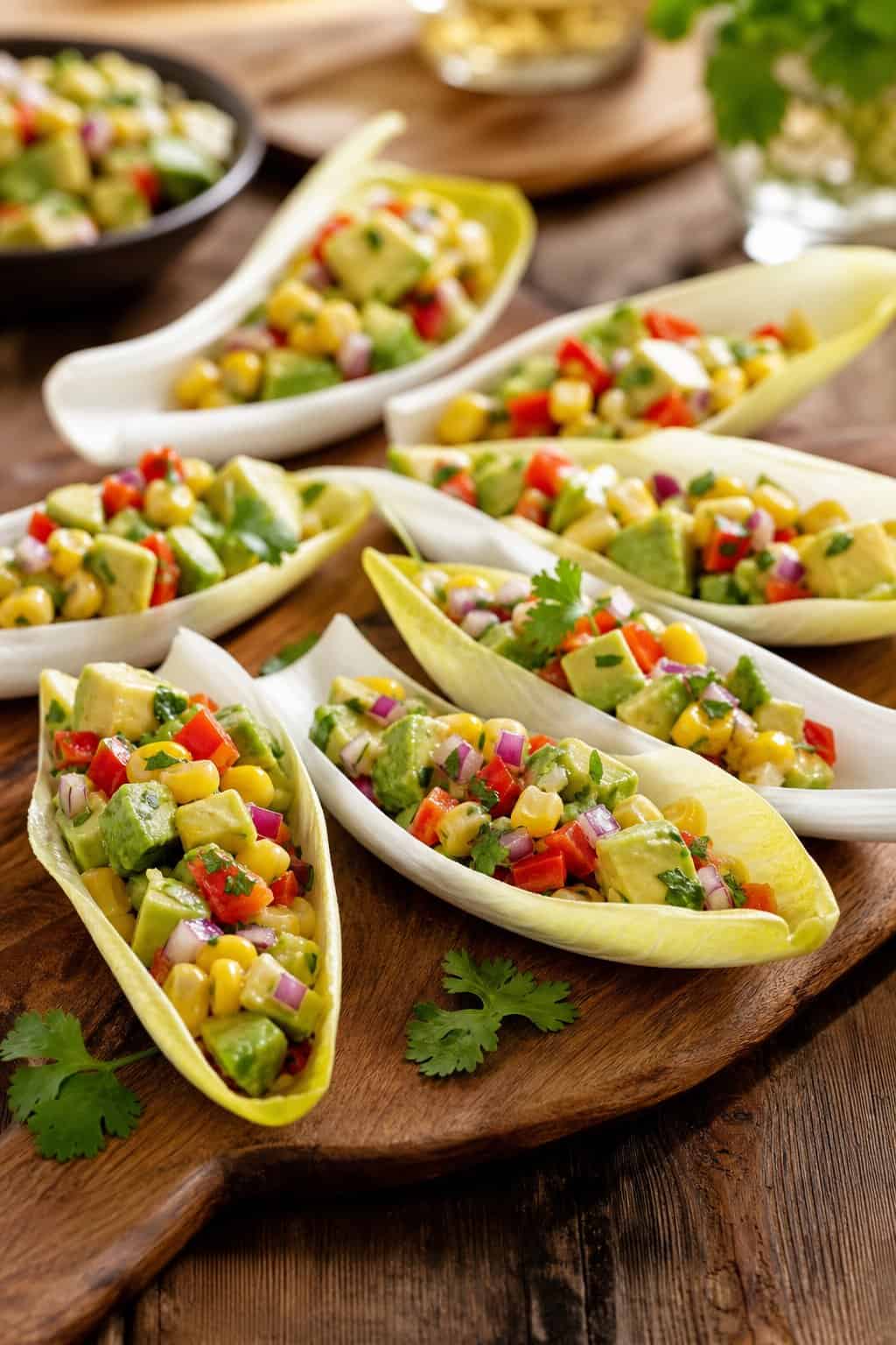 Endive spears filled with avocado corn salsa arranged on a wooden board.