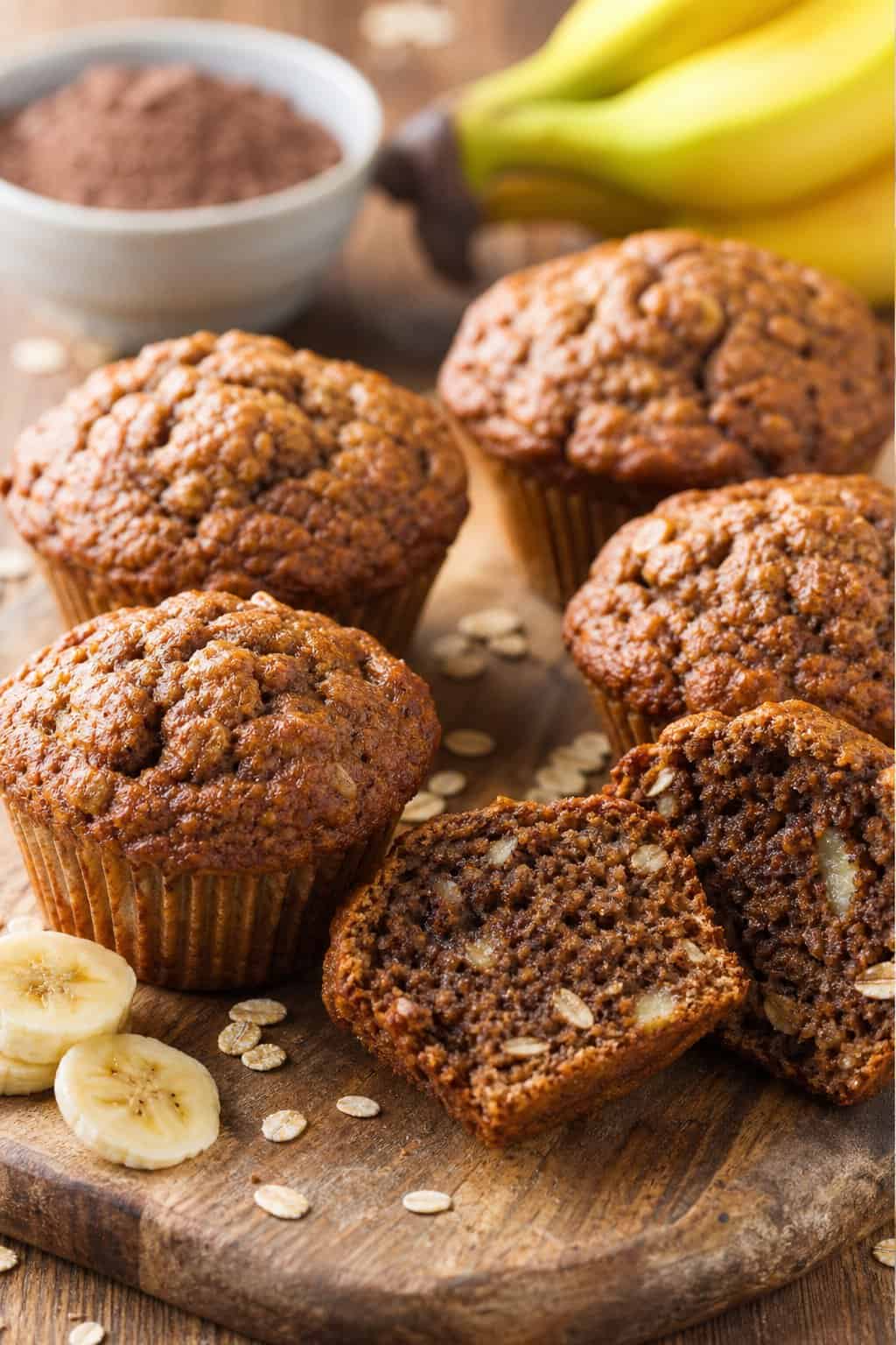 Freshly baked breakfast muffins made with brownie mix, oats, and banana arranged on a wooden board with banana slices and oats nearby.