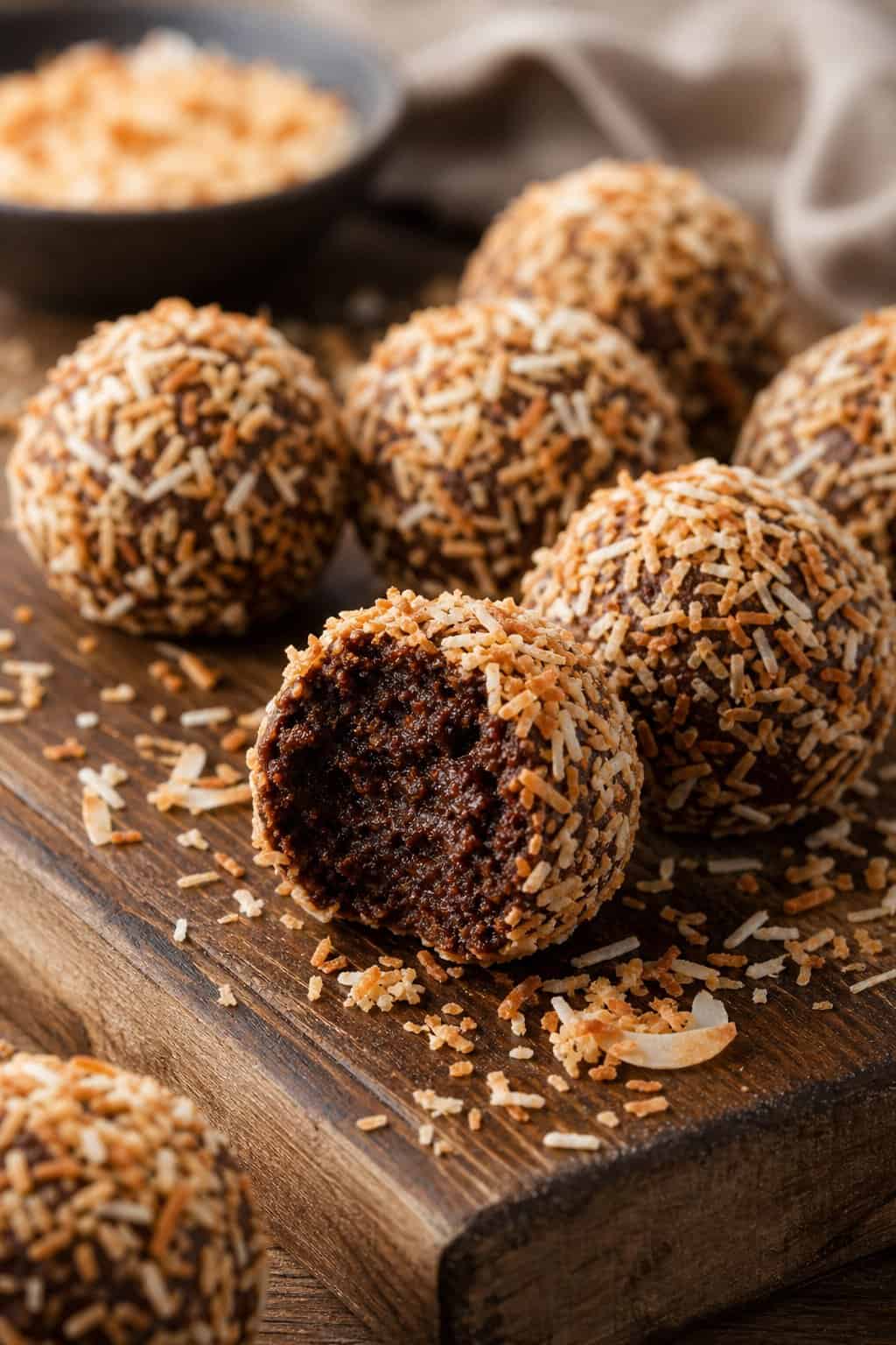 Close-up of chocolate brownie truffles rolled in toasted coconut arranged on a wooden board.