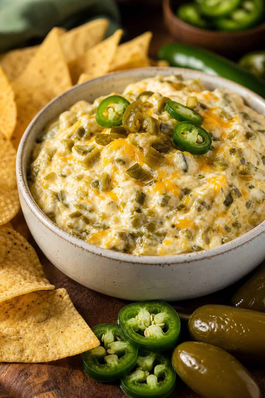 A bowl of creamy cheesy jalapeño popper dip with chopped jalapeños and tortilla chips on a wooden table.