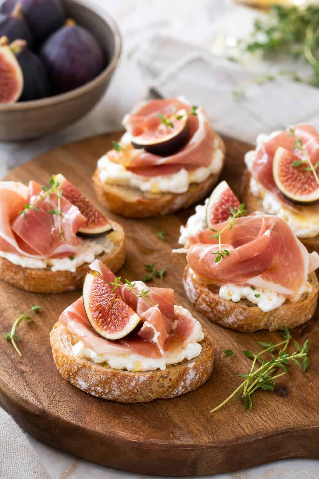 Close-up of prosciutto and fig crostini topped with mascarpone on a wooden serving board.