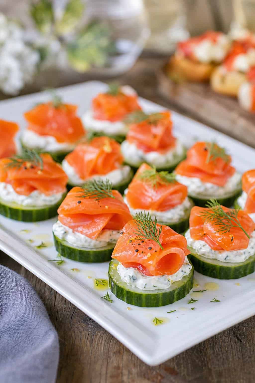A platter of cucumber slices topped with dill cream cheese and smoked salmon, garnished with fresh dill, on a wooden table.