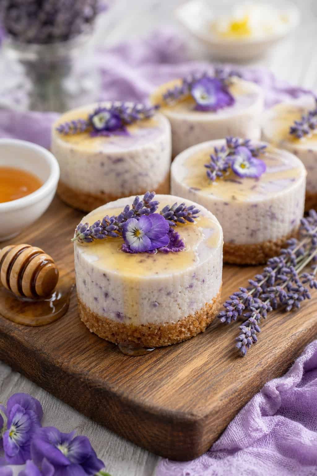 Several mini lavender honey cheesecakes on a wooden board, garnished with lavender sprigs and honey drizzle.