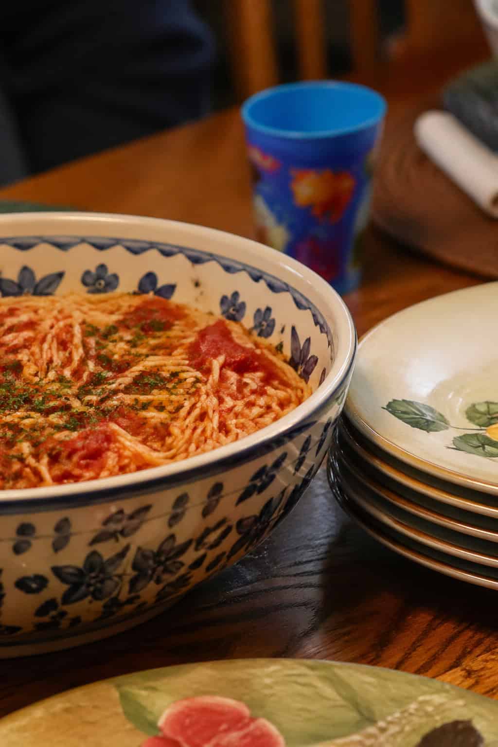 A large ceramic serving bowl filled with pasta on a wooden dining table