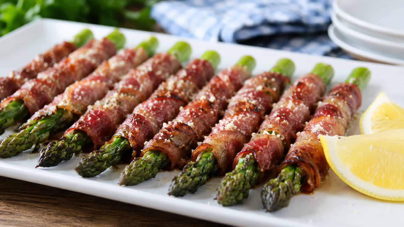crisp prosciutto-wrapped asparagus spears lined up on a long white platter in a wide horizontal shot, dusted with parmesan, lemon wedges on the side, bright natural light, shallow depth of field, landscape orientation