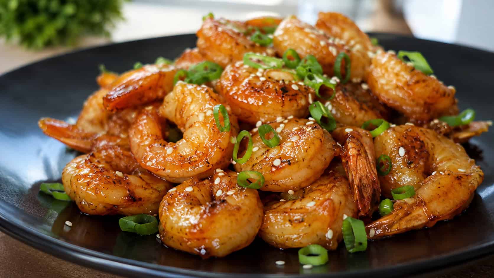 glossy honey garlic shrimp piled on a dark plate in a wide horizontal shot, glaze glistening, sliced scallions and sesame scattered on top, warm natural light, shallow depth of field, landscape orientation