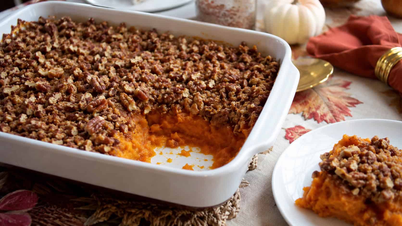 sweet potato casserole with a crunchy pecan topping in a wide horizontal shot, in a large baking dish with a scoop served on a plate on a holiday table, natural light, shallow depth of field, landscape orientation