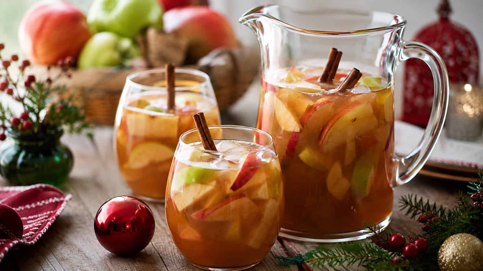 caramel apple sangria in a wide horizontal shot, in a glass pitcher and filled glasses with apple slices and cinnamon sticks on a festive holiday table, natural light, shallow depth of field, landscape orientation