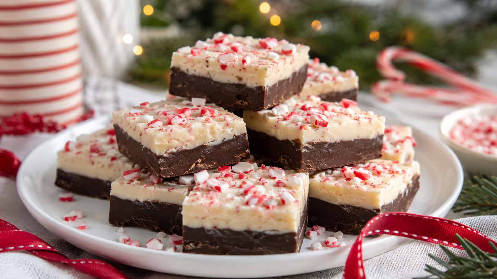 peppermint bark fudge squares in a wide horizontal shot, stacked on a white plate with crushed candy canes and a red ribbon on a festive holiday table, natural light, shallow depth of field, landscape orientation