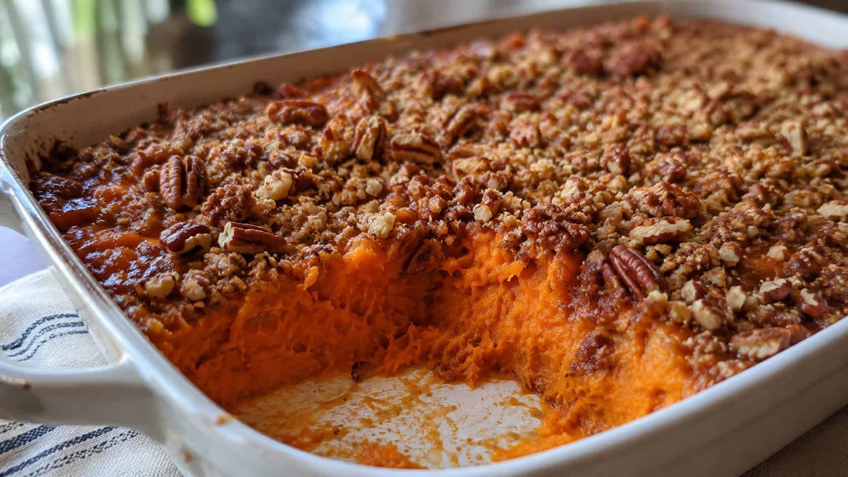 a sweet potato casserole with a golden crunchy pecan topping in a wide horizontal shot, served in a baking dish with a scoop removed, natural light, shallow depth of field, landscape orientation