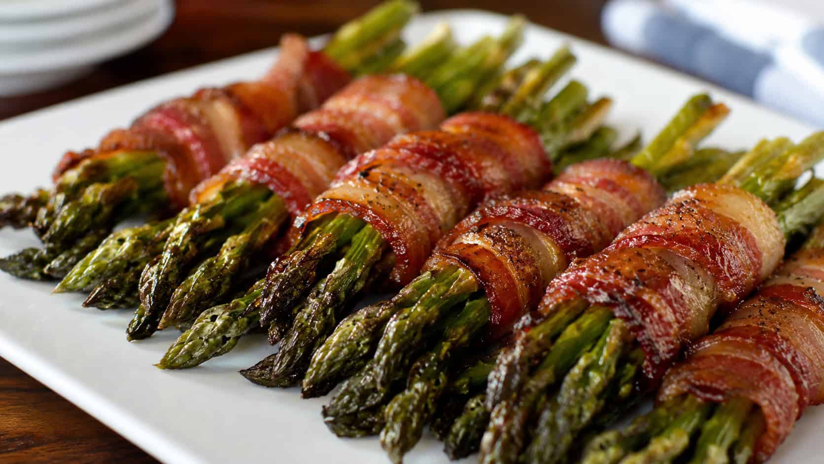 bacon-wrapped asparagus bundles with crisp glazed bacon in a wide horizontal shot, lined up on a serving platter, natural light, shallow depth of field, landscape orientation