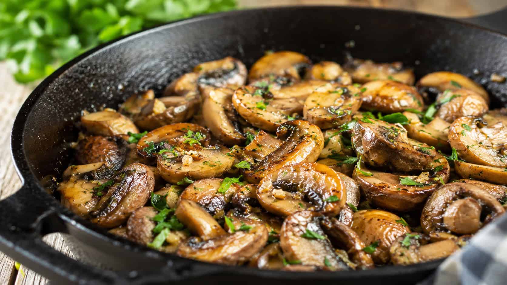 golden sauteed garlic mushrooms glistening with butter and parsley in a wide horizontal shot, served in a cast iron skillet, natural light, shallow depth of field, landscape orientation