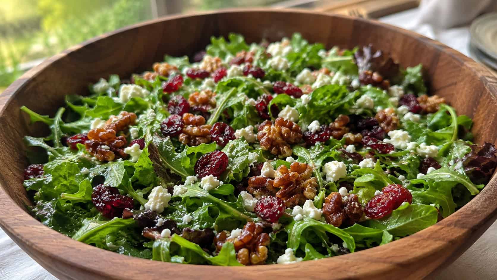 a cranberry walnut salad with greens, red cranberries, candied walnuts, and feta in a wide horizontal shot, served in a wide wooden bowl, natural light, shallow depth of field, landscape orientation