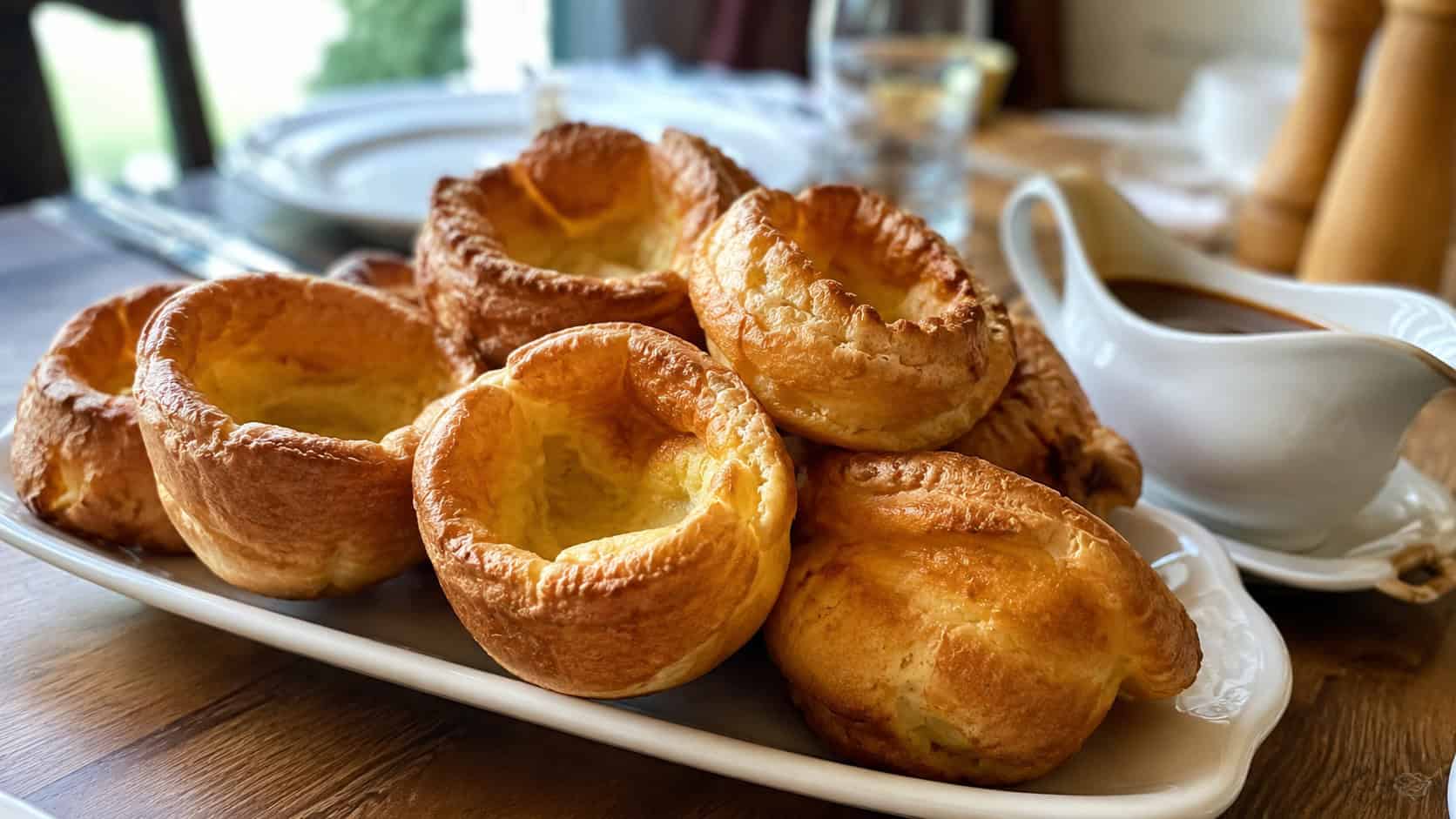 tall golden crisp Yorkshire puddings with hollow centers in a wide horizontal shot, arranged on a platter beside a gravy boat, natural light, shallow depth of field, landscape orientation