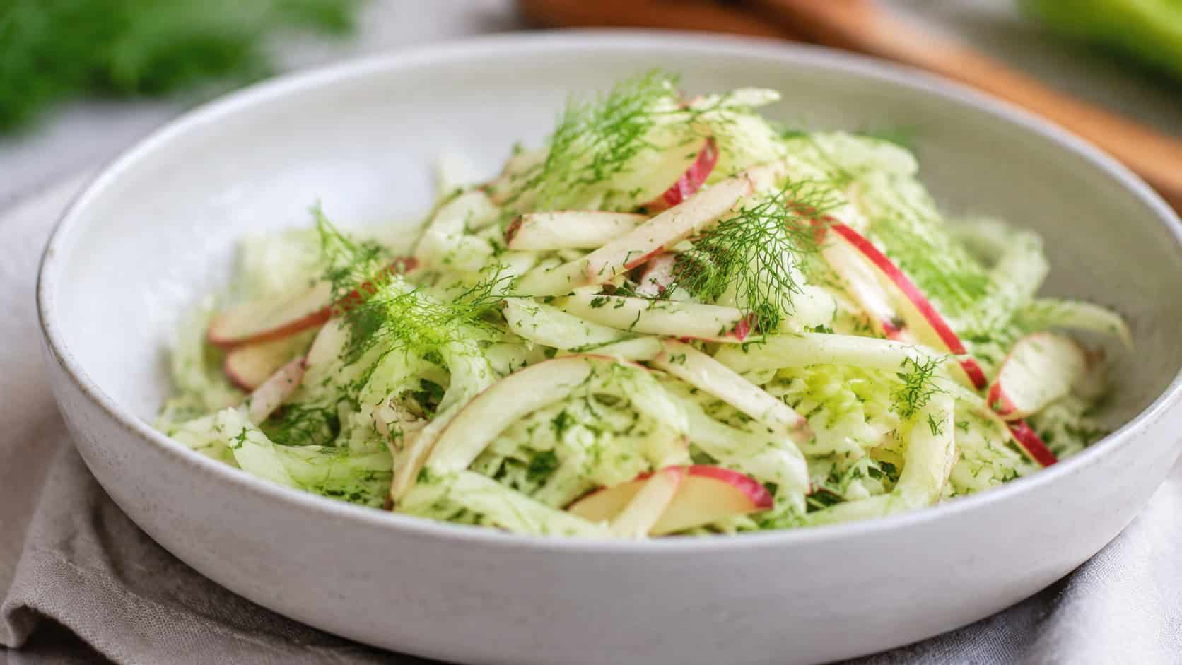 a crisp fennel and apple slaw with pale green and white ribbons in a wide horizontal shot, served in a shallow bowl with fennel fronds, natural light, shallow depth of field, landscape orientation