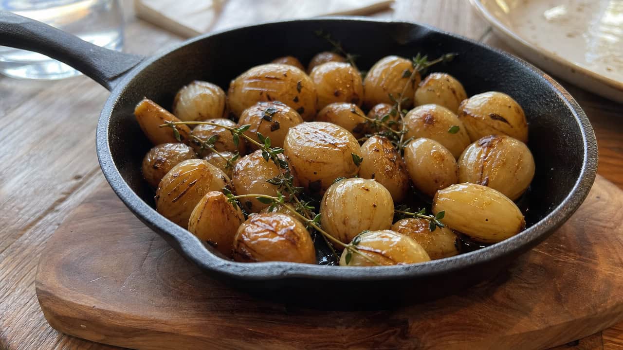 glossy caramelized pearl onions glazed in balsamic with thyme in a wide horizontal shot, served in a small skillet, natural light, shallow depth of field, landscape orientation