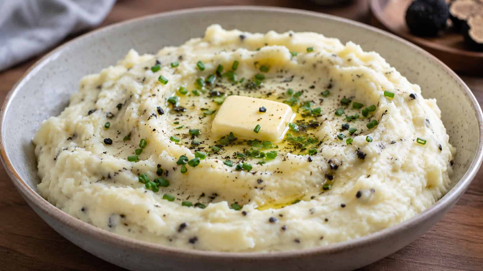 a bowl of creamy truffle mashed potatoes with a pat of melting butter and chopped chives in a wide horizontal shot, served in a wide bowl, natural light, shallow depth of field, landscape orientation