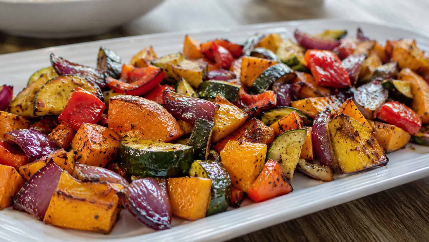 a colorful medley of honey balsamic roasted vegetables with squash, peppers, and onions in a wide horizontal shot, spread on a serving platter, natural light, shallow depth of field, landscape orientation