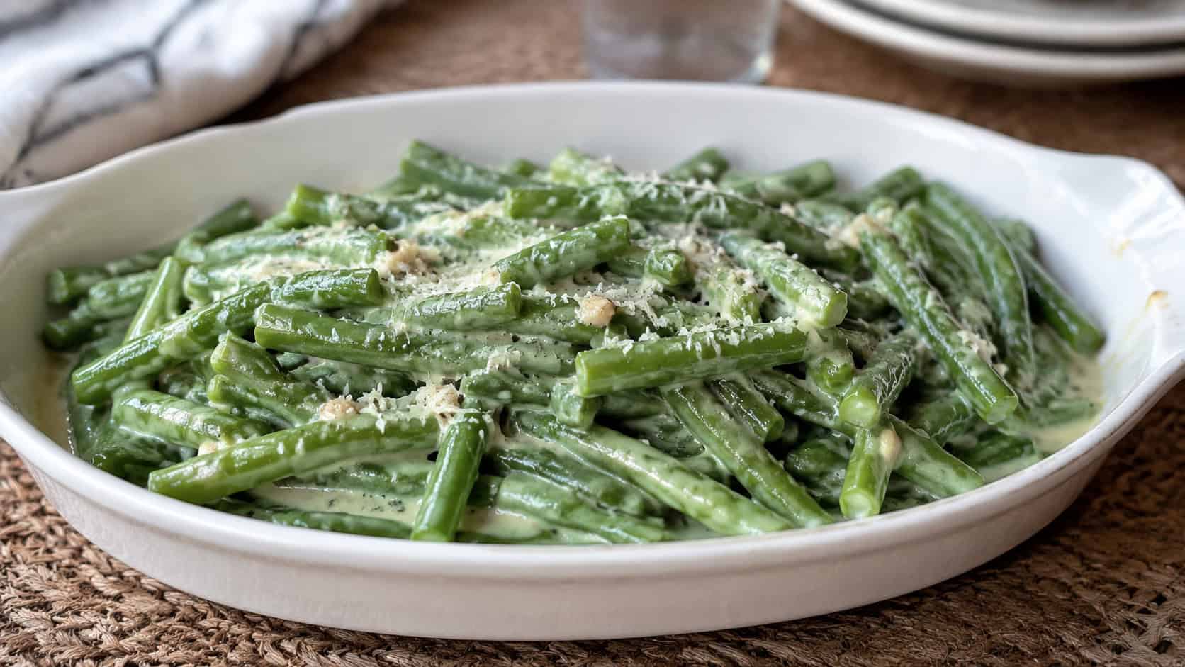 creamy garlic green beans glistening in Parmesan sauce in a wide horizontal shot, served in a white oval dish, natural light, shallow depth of field, landscape orientation