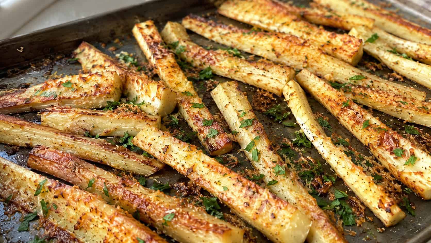 golden Parmesan roasted parsnip batons with a crispy cheesy crust in a wide horizontal shot, arranged on a baking tray sprinkled with parsley, natural light, shallow depth of field, landscape orientation