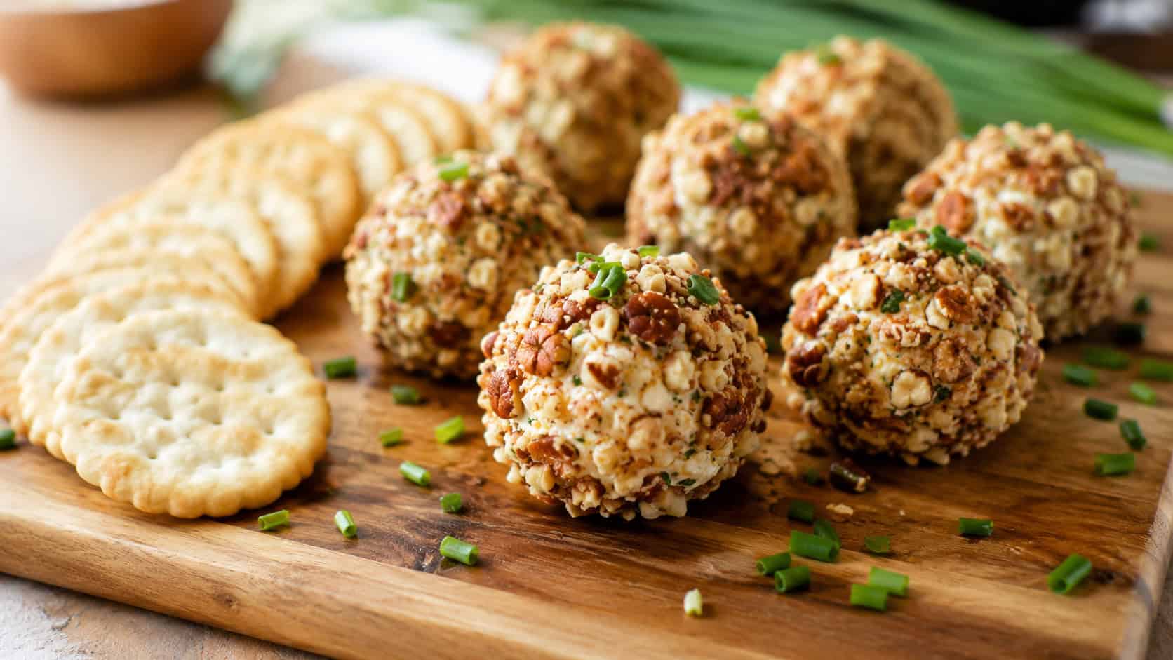 mini pecan-coated cheese balls on a wooden board in a wide horizontal shot, crackers fanned alongside, fresh chives scattered, warm natural light, shallow depth of field, landscape orientation