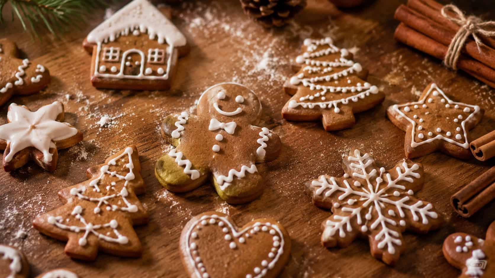 decorated gingerbread cookies with white icing on a wooden table in a wide horizontal shot, festive cutout shapes, scattered flour and cinnamon sticks, warm cozy natural light, shallow depth of field, landscape orientation