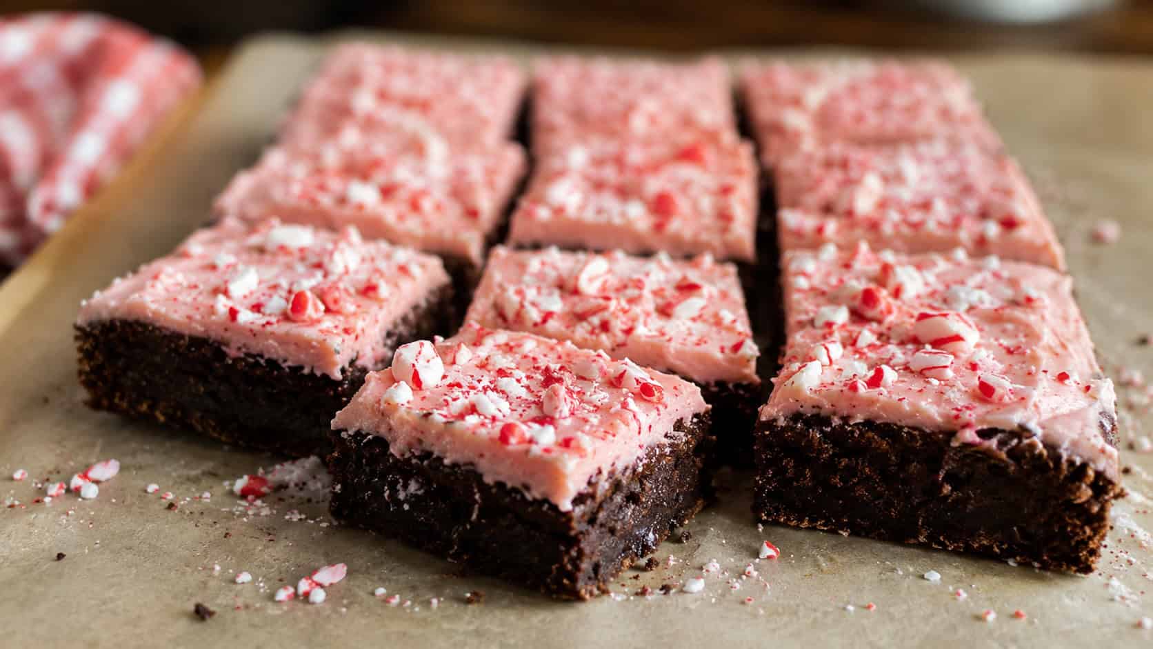 frosted candy cane brownies topped with crushed peppermint cut into squares on parchment in a wide horizontal shot, fudgy dark layer and pink frosting, scattered candy cane bits, warm natural light, shallow depth of field, landscape orientation