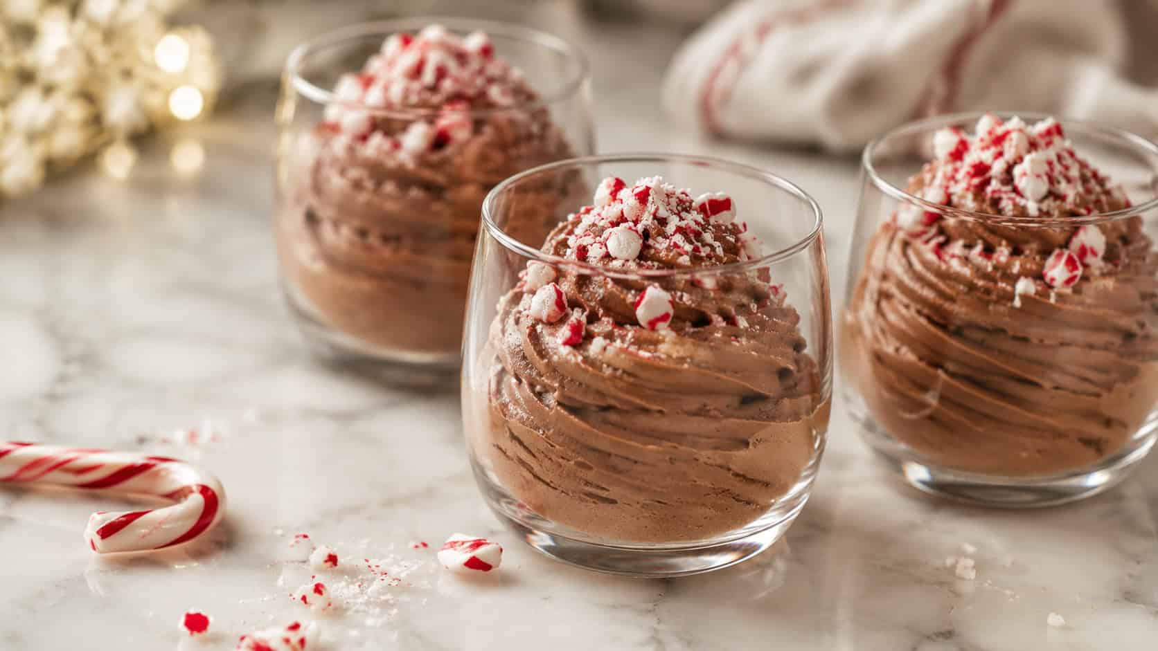 chocolate mousse piped into glasses topped with crushed red and white candy cane, in a wide horizontal shot on a marble counter with a few peppermint pieces nearby, soft elegant light, shallow depth of field, landscape orientation