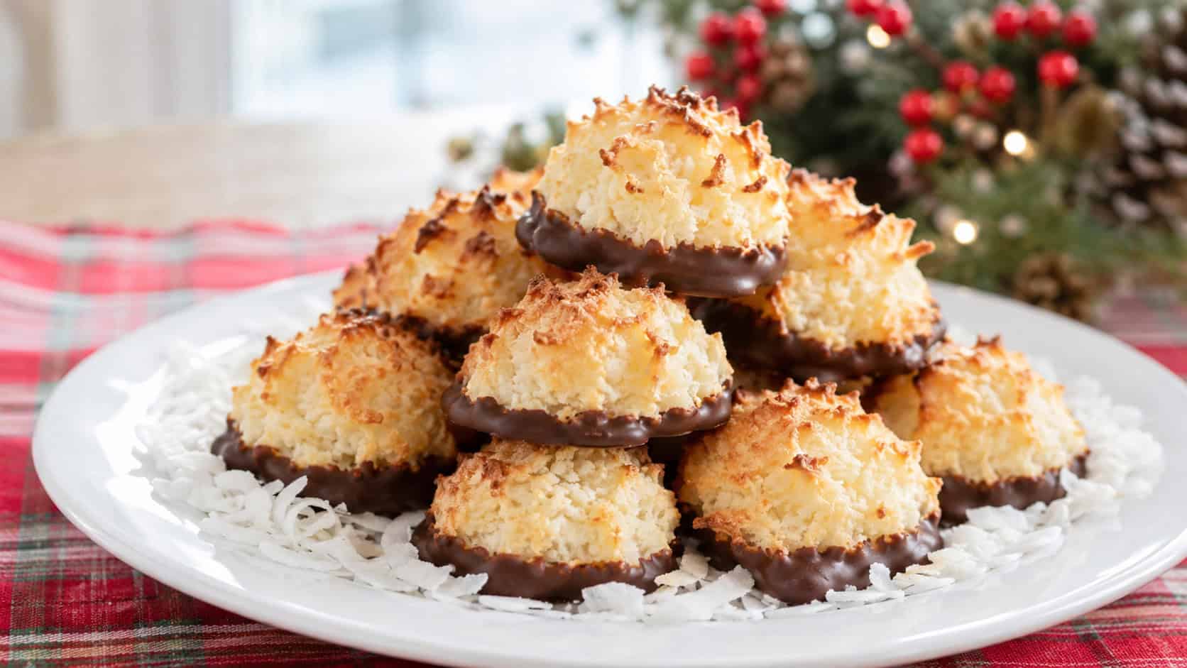 golden coconut macaroons with chocolate-dipped bottoms in a wide horizontal shot, piled on a white plate with shaved coconut around them on a festive table, natural light, shallow depth of field, landscape orientation