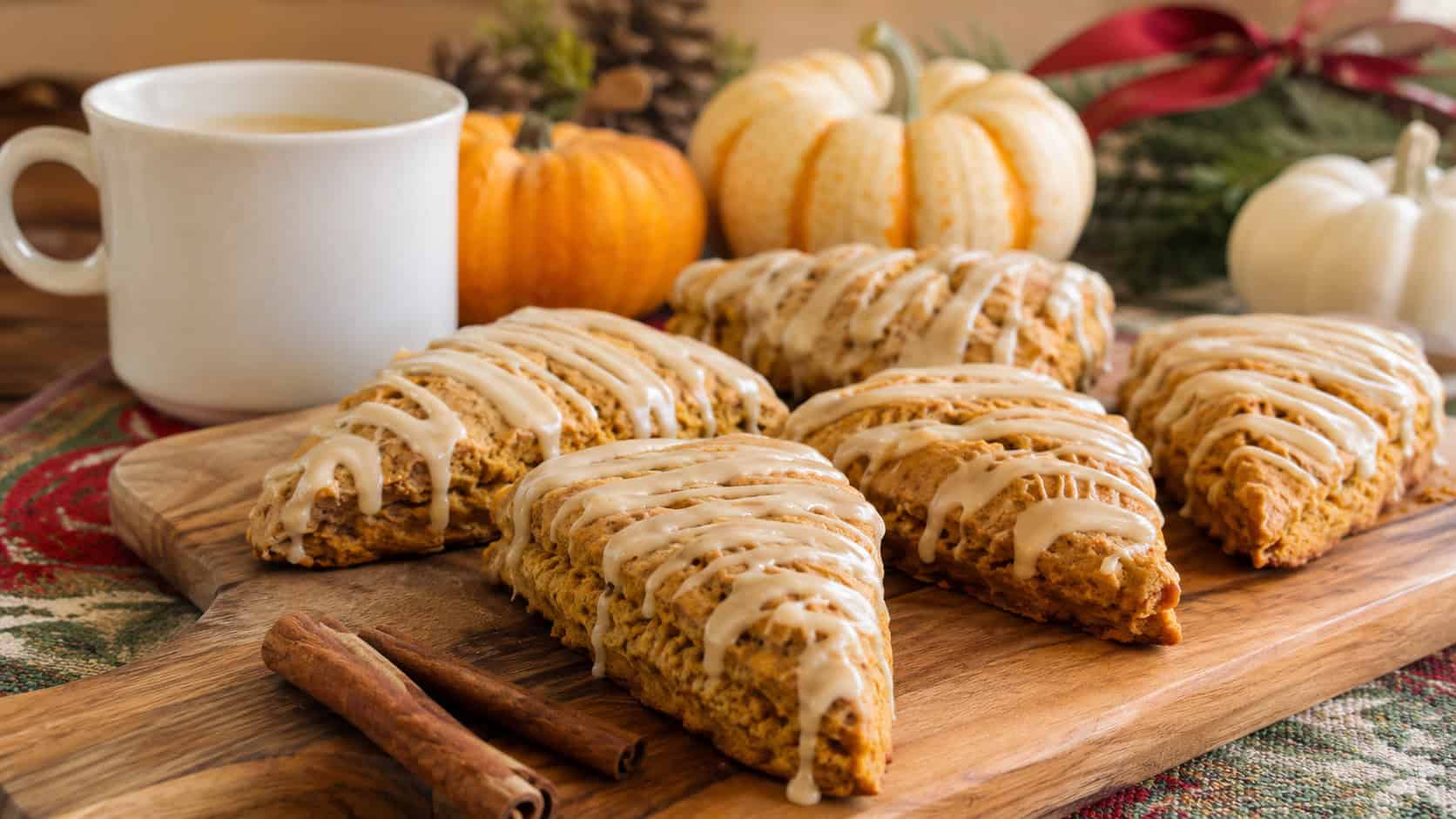 gluten-free pumpkin spice scones with maple glaze drizzle in a wide horizontal shot, arranged on a wooden board with cinnamon sticks and a coffee mug on a morning holiday table, natural light, shallow depth of field, landscape orientation