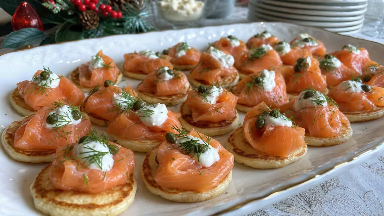 a platter of smoked salmon blinis topped with sour cream and dill in a wide horizontal shot, delicate salmon ribbons and capers, on a festive serving tray, bright natural light, shallow depth of field, landscape orientation