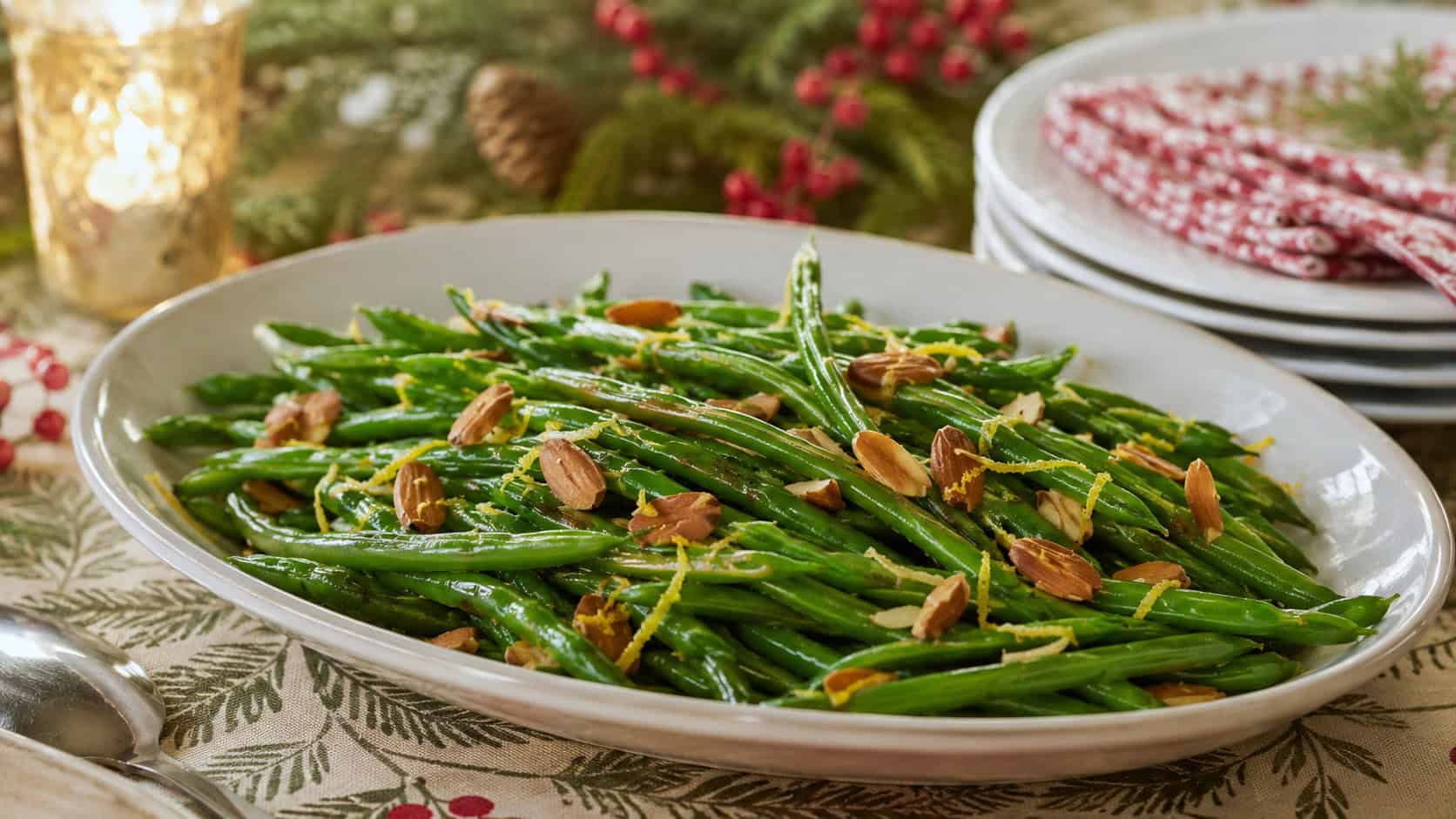 bright green beans tossed with golden toasted almonds and flecks of lemon zest, in a wide horizontal shot on an oval platter on a holiday table, warm natural light, shallow depth of field, landscape orientation