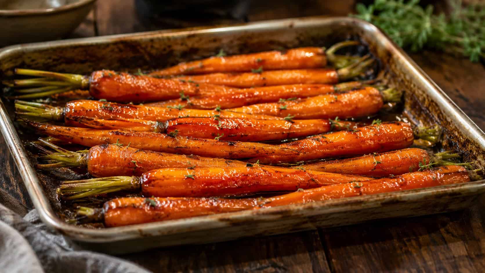 glossy maple-glazed whole carrots caramelized and flecked with thyme, in a wide horizontal shot on a roasting tray on a wooden table, warm rustic light, shallow depth of field, landscape orientation
