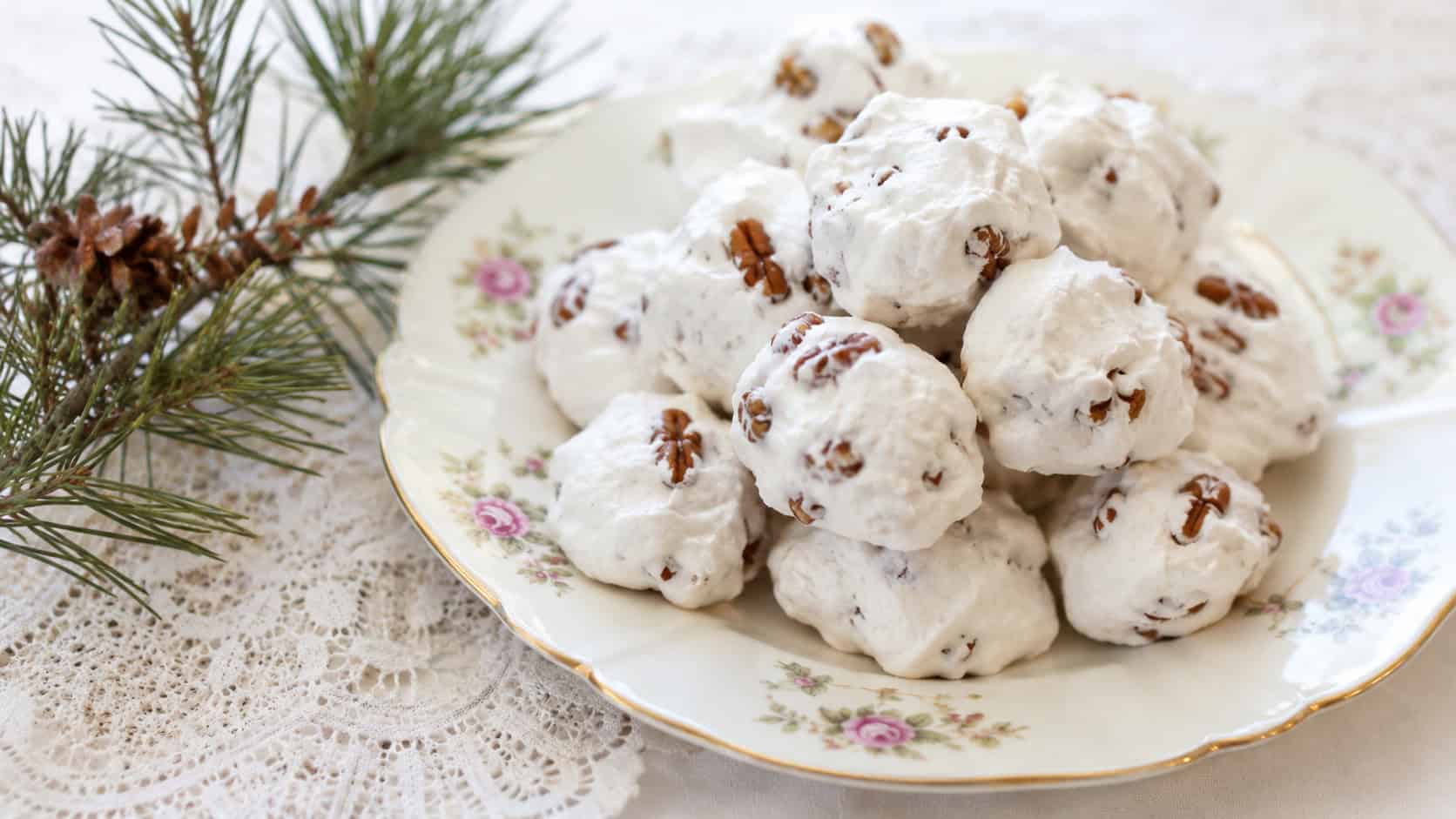fluffy white divinity candy dotted with pecans arranged on a vintage china plate in a wide horizontal shot, lace doily and pine sprigs beside it, soft bright natural light, shallow depth of field, landscape orientation