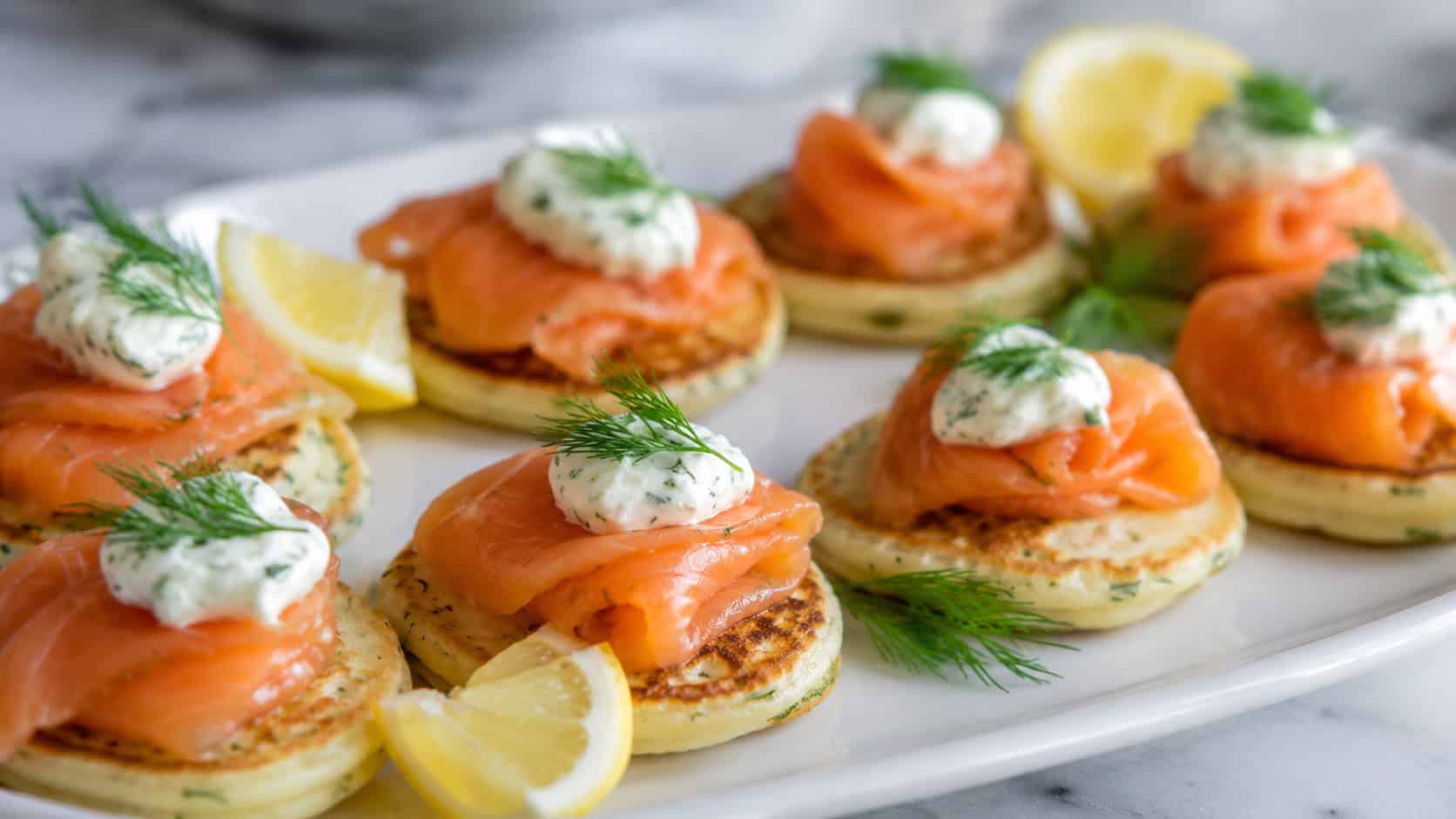 smoked salmon and dill blinis arranged on a white platter in a wide horizontal shot, creamy dollops and fresh dill, lemon wedges scattered around, soft natural light, shallow depth of field, landscape orientation
