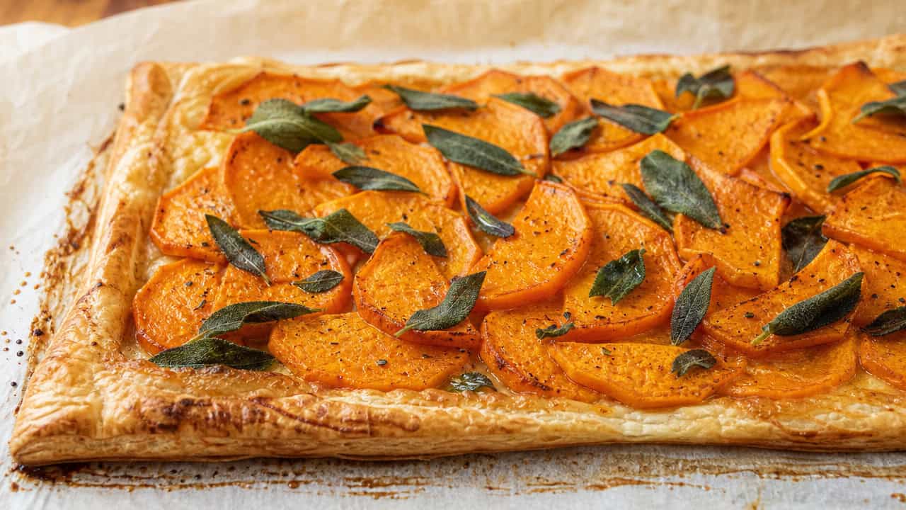 a rustic butternut squash and sage tart on parchment in a wide horizontal shot, overlapping orange squash slices and crisp sage, golden pastry edges, warm natural light, shallow depth of field, landscape orientation