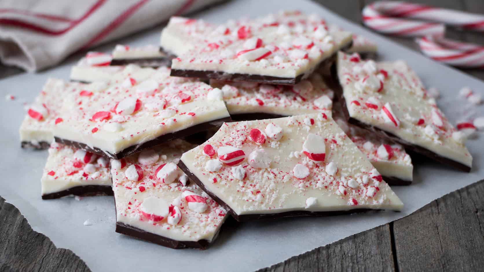 layered dark and white chocolate peppermint bark topped with crushed red and white candy broken into pieces, arranged in a wide horizontal shot on parchment over a rustic surface, cool natural light, shallow depth of field, landscape orientation