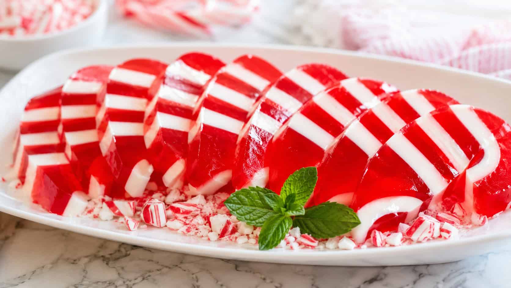 red-and-white striped peppermint jello slices that look like candy canes, in a wide horizontal shot fanned out on a white platter with crushed candy canes and a peppermint sprig, bright natural light, shallow depth of field, landscape orientation