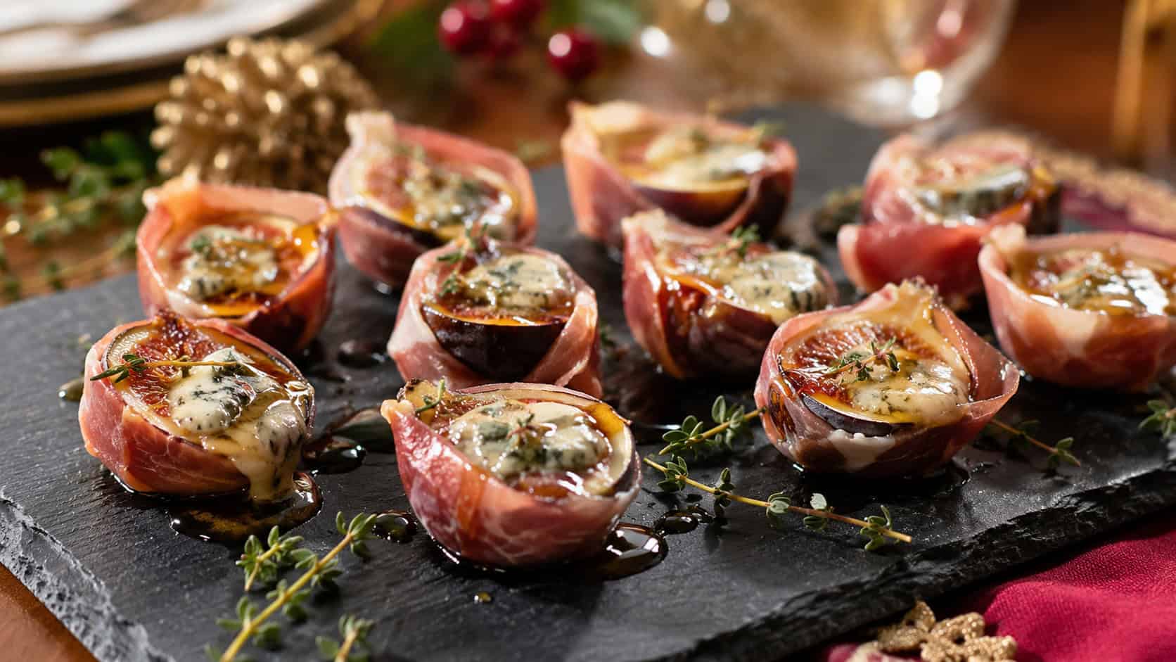 prosciutto-wrapped fig halves with melty gorgonzola, drizzled with honey and balsamic, shown in a wide horizontal shot arranged on a slate board with scattered thyme, on a festive table, warm natural light, shallow depth of field, landscape orientation