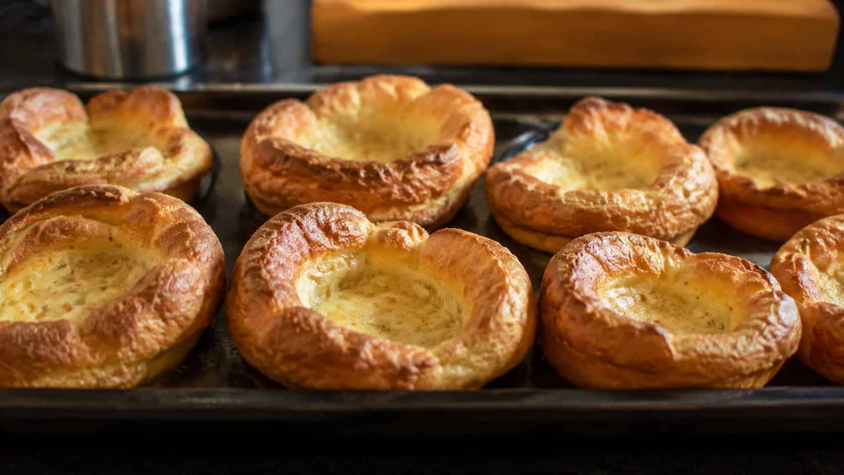 golden puffed Yorkshire puddings lined up wide across a baking tray, crisp risen edges visible, warm natural light, shallow depth of field, horizontal landscape composition